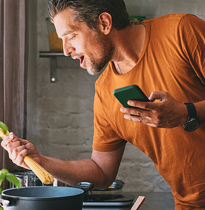 http://Imagem%20de%20um%20homem%20cozinhando%20macarrão,%20com%20o%20celular%20na%20mão.